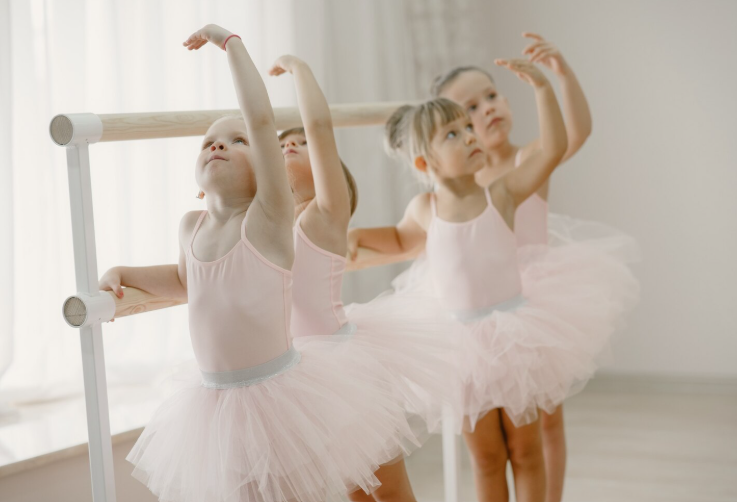 Niñas pequeñas practicando preballet en barra de danza